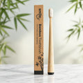 Smile Dew bamboo toothbrush with white soft bristles and a black base, standing beside its branded kraft box on marble.