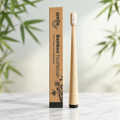 Smile Dew bamboo toothbrush with white soft bristles and a black base, standing beside its branded kraft box on marble.